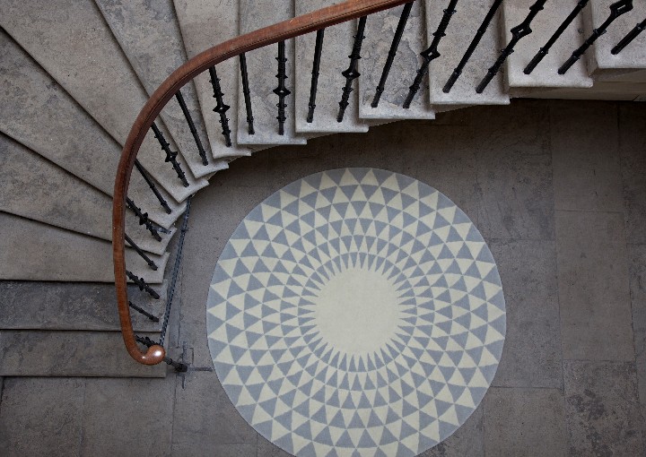 An aerial shot grey and cream circular rug with a geometric pattern next to a curved staircase